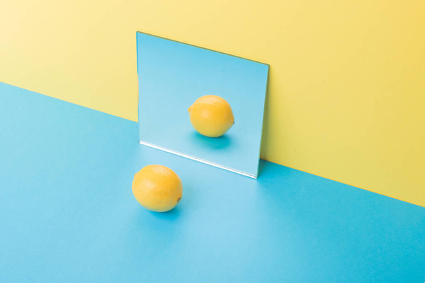Lemon on blue table isolated over yellow background near mirror - Photo, Image