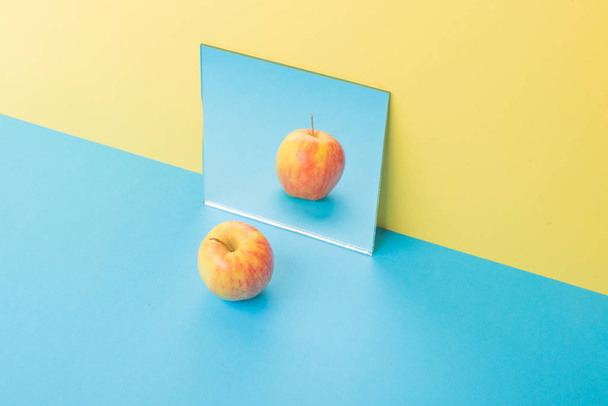 Apple on blue table isolated over yellow background near mirror - Фото, зображення