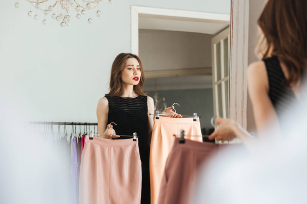 Joven mujer concentrada de pie en la tienda eligiendo ropa
 - Foto, Imagen