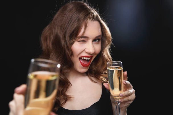 Cheerful young woman giving you glass of champagne and winking - Foto, imagen