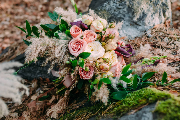 Beautiful wedding bouquet consisting of different flowers lying on a stone in the park. Autumn wedding - Photo, Image