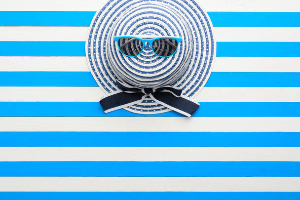 Ριγέ καπέλο και γυαλιά ηλίου σε μπλε-λευκό φόντο. Το Top view, επίπεδη lay. - Φωτογραφία, εικόνα