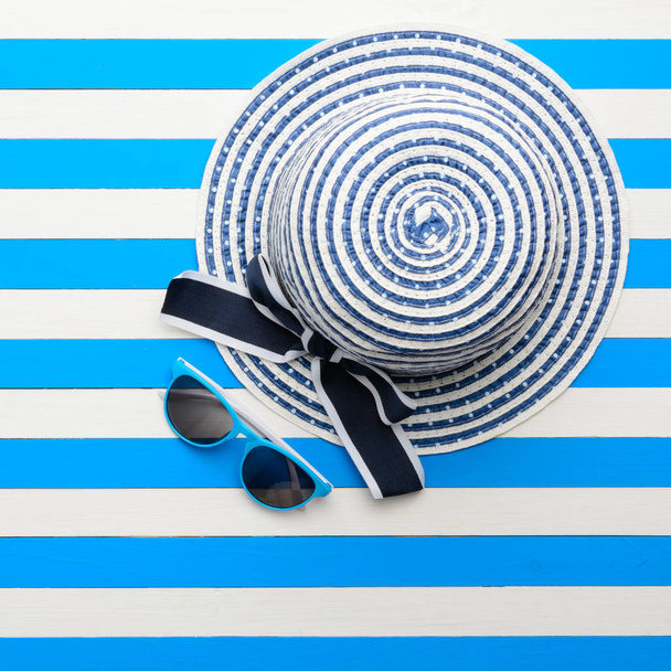 Striped hat and sunglasses on blue-white background. Top view, flat lay. - Photo, Image