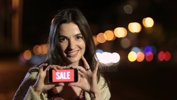 Dziewczyna trzyma telefon z sprzedaż reklam na ekranie w nocy - Materiał filmowy, wideo