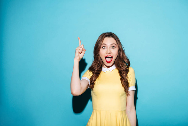 Beautiful excited girl in dress pointing finger up at copyspace - Foto, Imagem