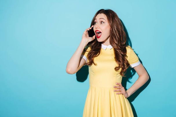 Happy young brunette woman in yellow dress talking by phone. - Fotó, kép