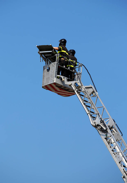 Dos intrépidos bomberos sobre la canasta de metal del camión de escalera dur
 - Foto, Imagen