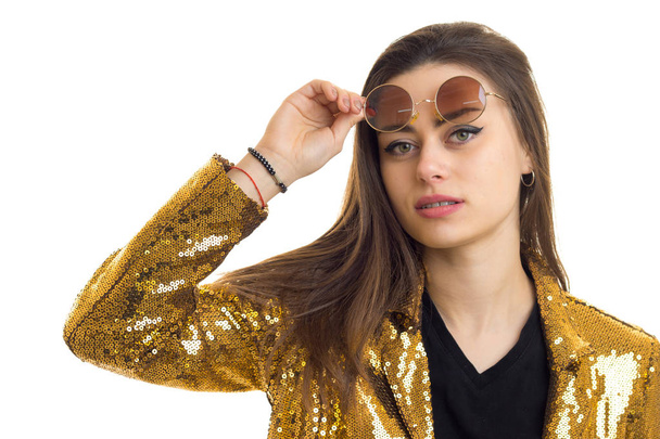 close up portrait of pretty brunette woman in round sunglasses and golden jacket looking at the camera - Foto, imagen