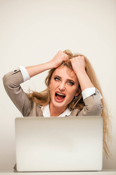 Angry businesswoman sitting in front of her laptop with her hands holding her hair. - Foto, immagini