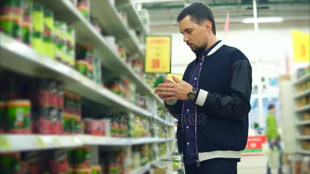 Mężczyzna w średnim wieku patrzy na żywność w puszkach, w sklepie spożywczym z zainteresowaniem - Materiał filmowy, wideo