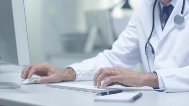 Close-up of a White Haired Senior Doctor and His Assistant Working at Desktop Computers. Working in Brightly Lit Office. - Πλάνα, βίντεο