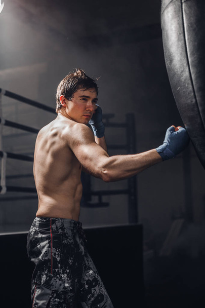 Man practicing boxing on big black bag in gym - Fotó, kép