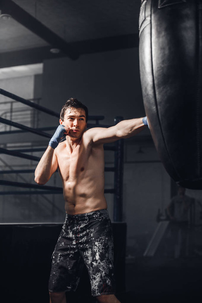 Male boxer boxing in punching bag in a sport gym - Φωτογραφία, εικόνα