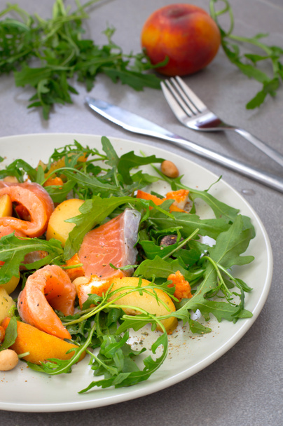 Salad with salmon, arugula, peach and peanuts. Rustic style. Gray stone background. Close-up. Top view - Photo, Image