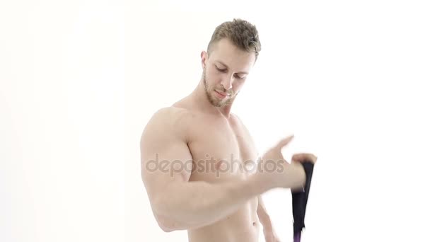 Medium shot of a muscular bodybuilder doing arm exercises with a resistance band on a white background - Footage, Video