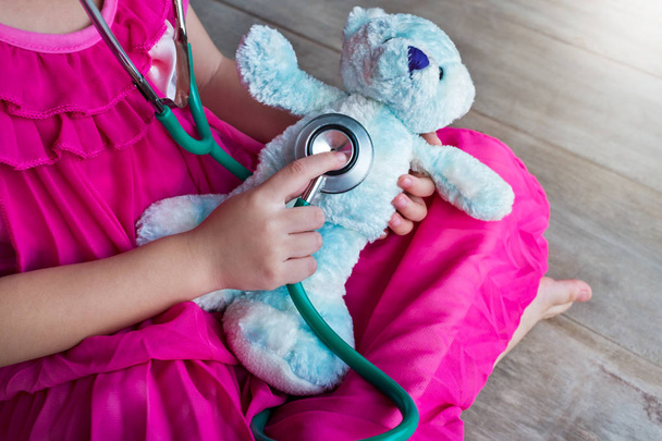 Дитина грає у лікаря або медсестру з плюшевим іграшковим ведмедем вдома
.  - Фото, зображення