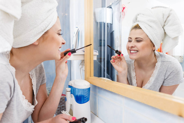 Woman in bathroom applying mascara on eyelashes - Valokuva, kuva