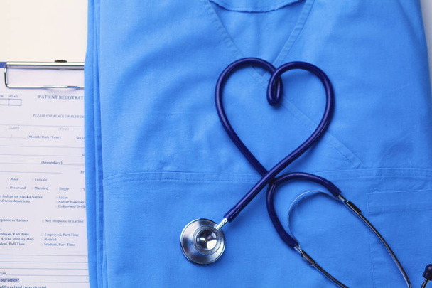 Stetoscopio medico attorcigliato a forma di cuore che giace sulla lista anamnesi del paziente e primo piano uniforme medico blu
 - Foto, immagini