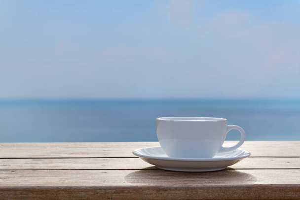 Copa de café blanco en la mesa de madera con fondo borroso cielo marino
 - Foto, imagen