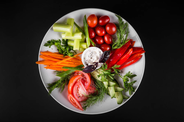 Assortment of fresh vegetables on a plate. On a dark background, top view. - Foto, afbeelding