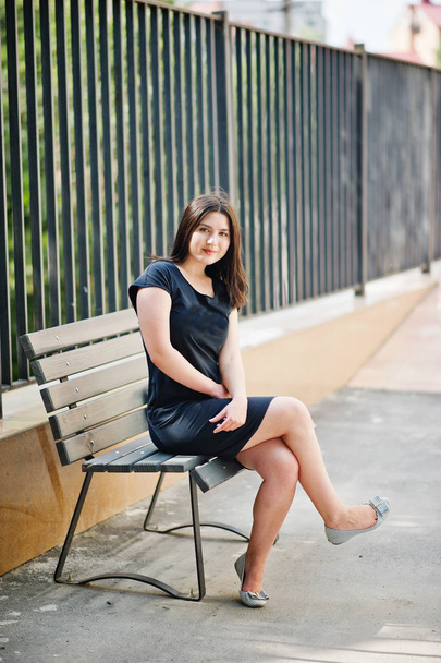 Brunette girl at black dress sitting on bench and posing at stre - Foto, imagen