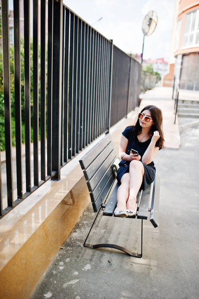 Brunette girl at black dress, sunglasses sitting on bench, liste - Fotografie, Obrázek