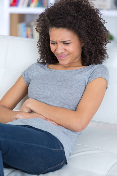 Young woman on sofa with stomach pain - Zdjęcie, obraz