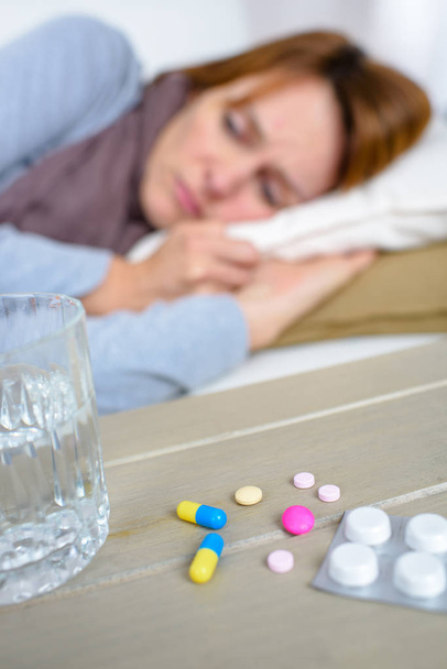 Женщина лежала на диване рядом с ассортиментом таблеток и воды
 - Фото, изображение
