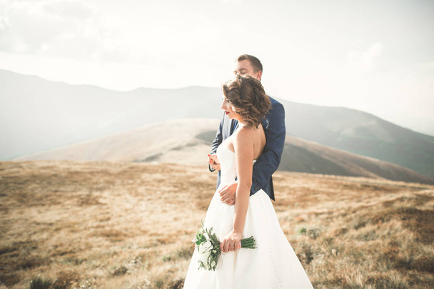 Beautifull wedding couple kissing and embracing near mountain with perfect view - Фото, зображення