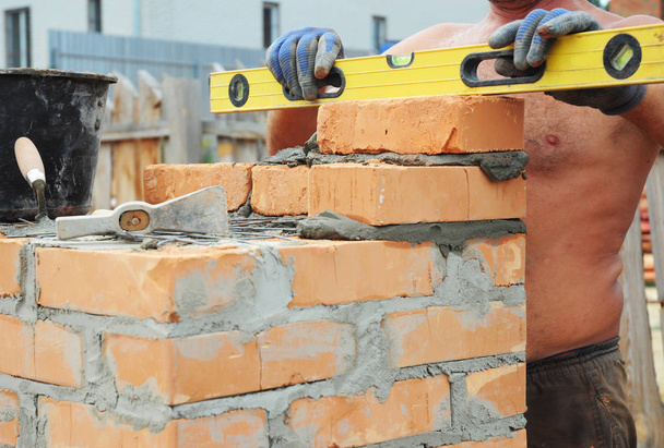 Bricklayer Bricklaying Concept (em inglês). Ferramentas de assentamento de tijolos. Um pedreiro usando um nível para verificar sua nova parede de construção da casa ao ar livre. Tijolos. assentamento de tijolos, pedreiro, alvenaria
.  - Foto, Imagem