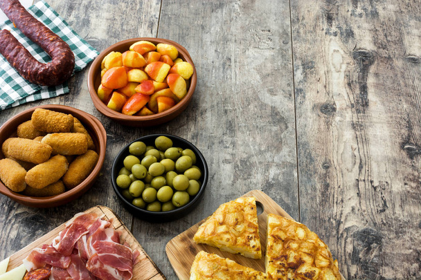 Traditionele Spaanse tapas. Kroketten, olijven, omelet, ham en patatas bravas op houten tafel - Foto, afbeelding