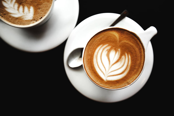Kaksi kuppia cappuccinoa mustalla pöydällä
 - Valokuva, kuva