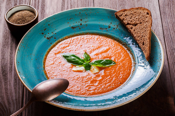 Tomato gazpacho soup with basil, feta cheese, ice and bread on dark wooden background, Spanish cuisine. Ingredients on table. Top view - Photo, Image