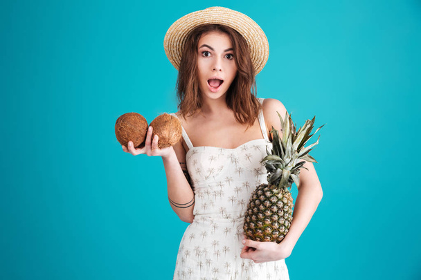 Girl in summer clothes holding two coconuts and pineapple - Photo, Image