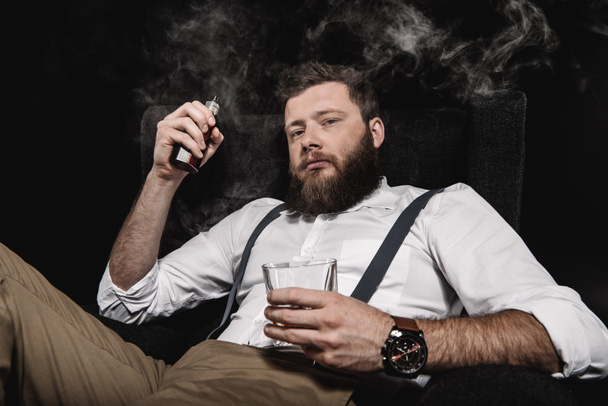 stijlvolle man vaping met whisky glas  - Foto, afbeelding