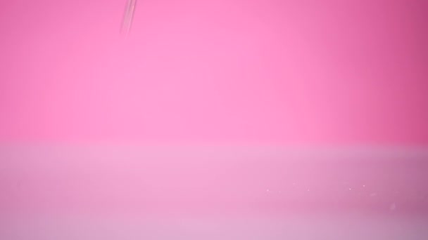 A broken egg falls on the table on the pink background - Felvétel, videó