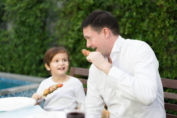 Father with little bcute boy eating barbecue in family lunch tim - Photo, image