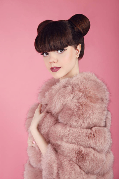 Beauty bun hairstyle.  Fashion teen girl model in pink fur coat. - Foto, afbeelding