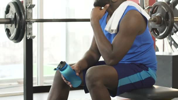 Genç erkek spor salonunda oturmuş yüzünü havluyla siliyor şişe su tutarak - Video, Çekim