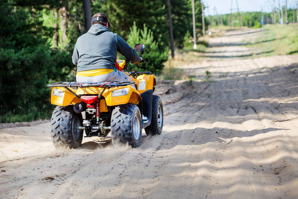Um homem montando ATV em uma estrada de areia, vista traseira
 - Foto, Imagem