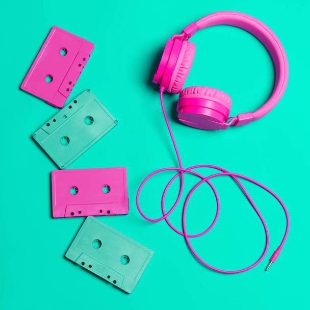 Pink headphones and audio cassettes with CDs on a turquoise background - Фото, изображение