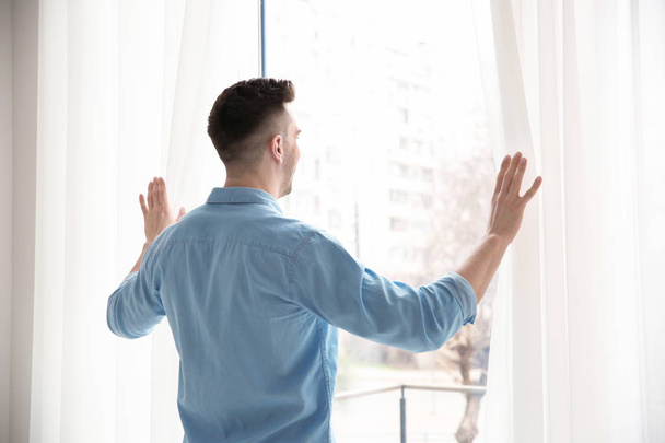 man opening curtains - Foto, afbeelding