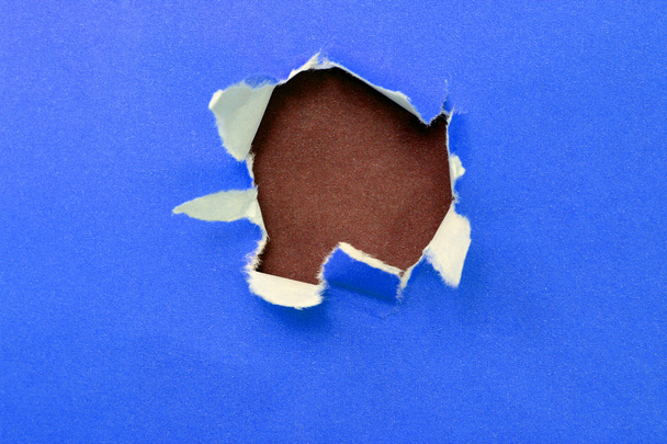 hole in the blue paper with ragged edges and brown texture - Photo, Image