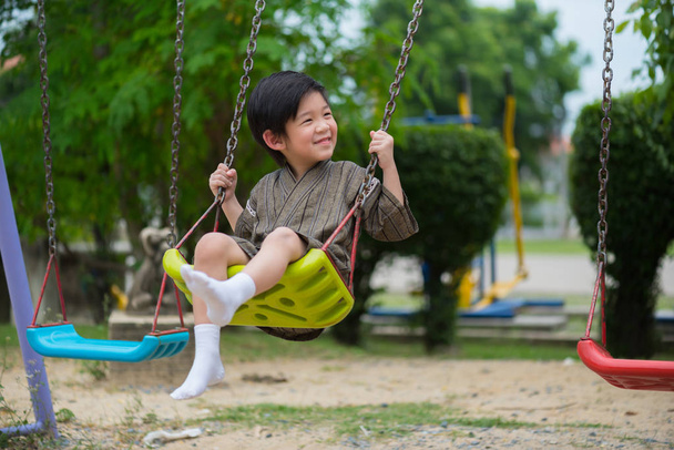 primer plano de feliz asiático chico desgaste japonés paño jugando swing en parque
. - Foto, Imagen