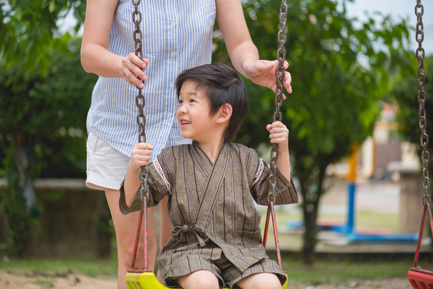 Lähikuva onnellinen aasialainen poika leikkii keinu äidin kanssa puistossa
. - Valokuva, kuva