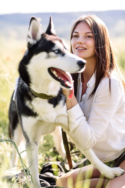 Beautiful girl plays with a dog (black and white husky with blue eyes) green field - Photo, Image