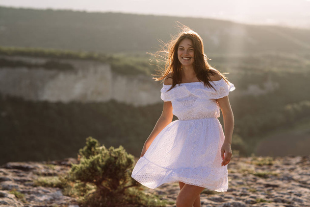 Beautiful girl remains on top of a mountain and looks at the horizon with a beautiful background. A colorful photo of a natural sunset, a miracle, incredible, a dance, hair in the wind - Фото, изображение