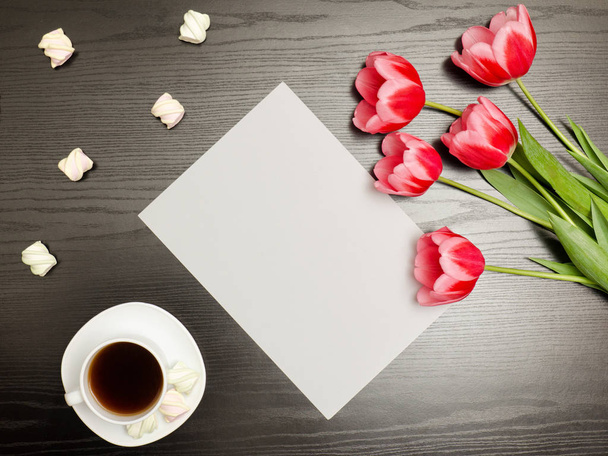 Ein sauberes Blatt Papier, rosa Tulpen und eine Tasse Kaffee. schwarzer Tisch. Ansicht von oben - Foto, Bild
