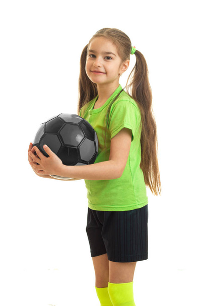 vertical portrait of cutie little girl in green shirt holding a soccer ball in hands - Фото, изображение