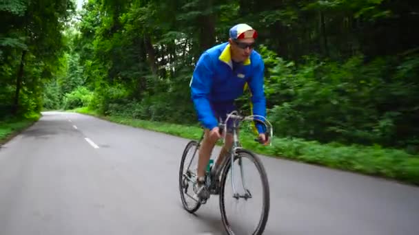 Middle-aged man is riding a road bike along a forest road - Footage, Video